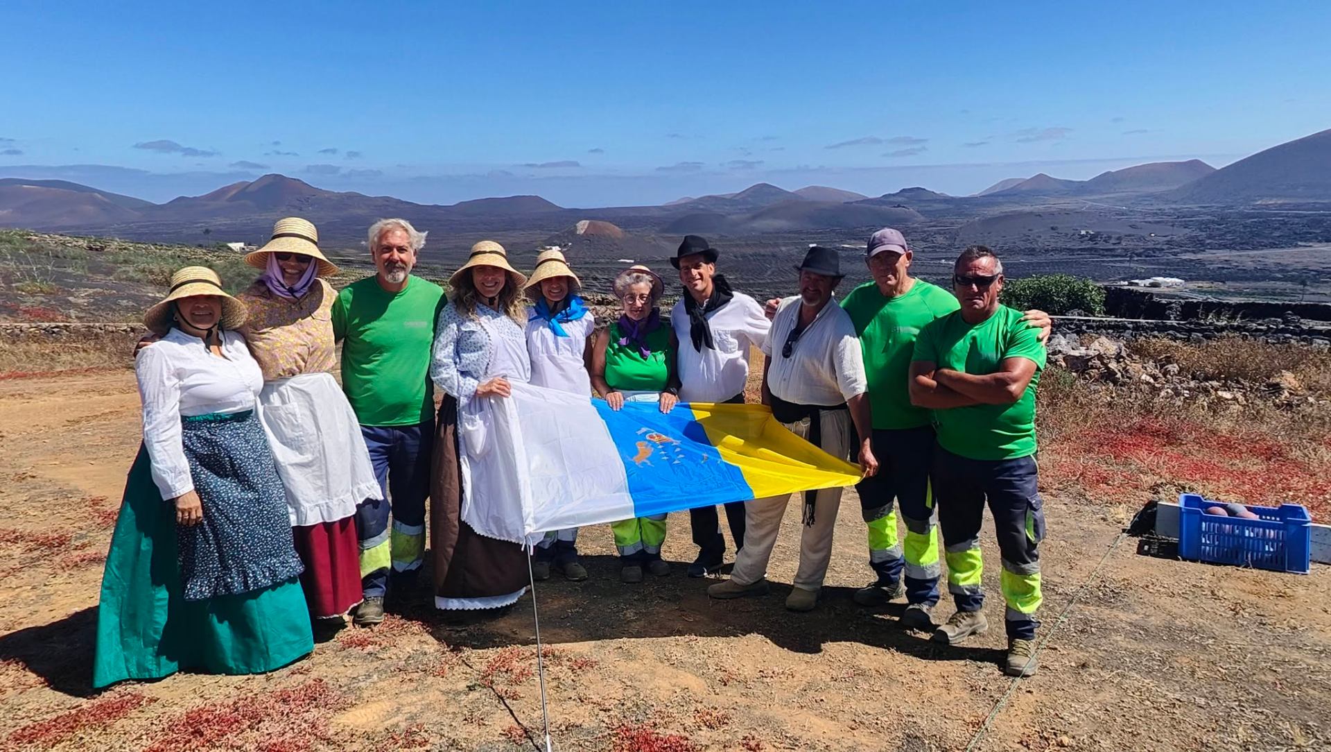 Equipo posando con bandera canaria en el paisaje de viñedos con los volcanes de Lanzarote al fondo