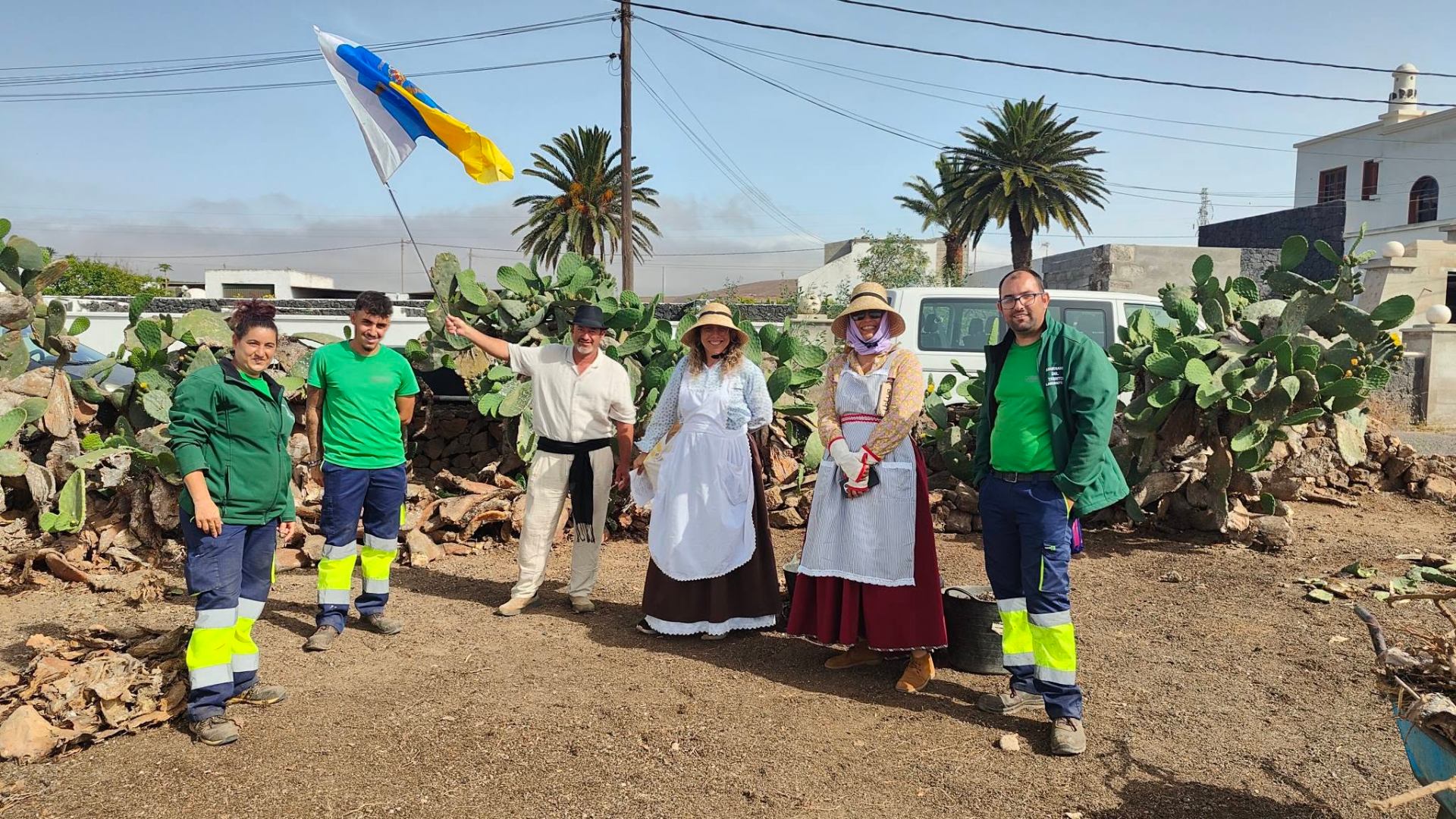 Equipo posando con bandera canaria entre tuneras y palmeras en Lanzarote