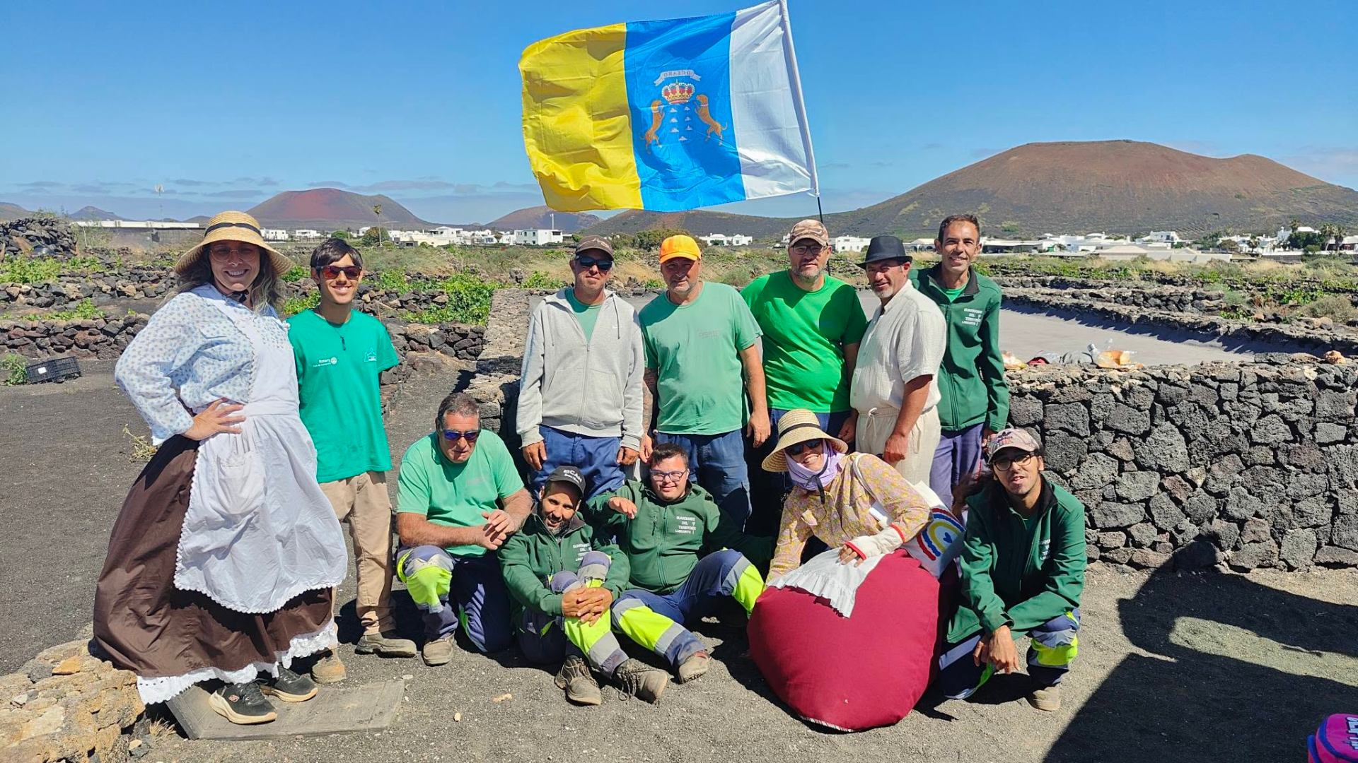 Equipo posando bajo la bandera canaria ondeando al viento con un volcán al fondo
